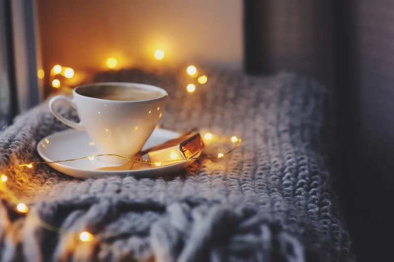 A cup of tea on a knitted blanket, with soft fairy lights